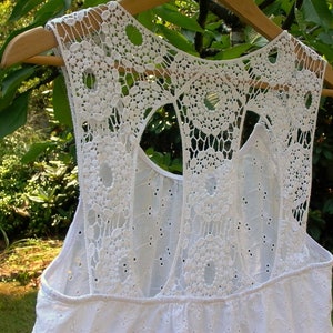 May include: White crochet top with a lace back and a cutout design. The top has a sleeveless design and a relaxed fit.