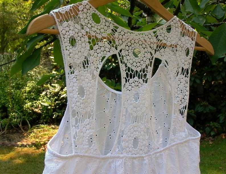 May include: White crochet top with a lace back and a cutout design. The top has a sleeveless design and a relaxed fit.