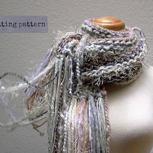 May include: A white, gray, and brown knitted scarf with long, frayed strands hanging from the bottom. The scarf is displayed on a white mannequin.