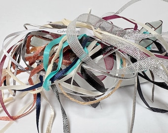 May include: A tangled assortment of ribbons in various colors and textures. Ribbons include satin, mesh, and grosgrain in shades of silver, black, teal, burgundy, and cream. A small white ribbon with the text "Calvin Klein" is visible.