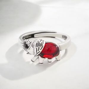 May include: A silver ring featuring a red gemstone shaped like an elephant. The ring is adjustable and has the number "925" engraved on the band.