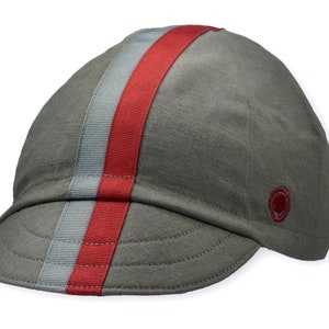 Le Pave Cycling Cap,
A four-panel, Gray linen/cotton hat with a short brim. Gray and burgundy ribbon runs from the back of the cap to the bottom of the brim. Red Dots embroidered burgundy logo on the side panel.