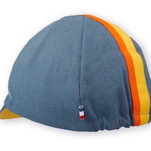 Race to the Sun Cycling Cap by Red Dots Cycling.
A four-panel, vintage blue linen/cotton hat and yellow under brim. Yellow and orange ribbon to the top of the brim. A vintage blue Red Dots embroidered logo and 3-color French ribbon on side panel.