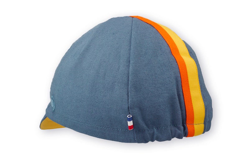 Race to the Sun Cycling Cap by Red Dots Cycling.
A four-panel, vintage blue linen/cotton hat and yellow under brim. Yellow and orange ribbon to the top of the brim. A vintage blue Red Dots embroidered logo and 3-color French ribbon on side panel.