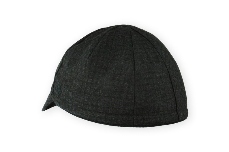 Equinox Winter Cap by Red Dots Cycling. Detail of black, double-layered, bamboo cotton ribbed ear flap in up position. Short brim, 100% wool plaid fabric, charcoal grey/black plaid and purple accent. Red Dots black logo embroidered on side panel.