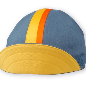 Race to the Sun Cycling Cap by Red Dots Cycling.
A four-panel, vintage blue linen/cotton hat and yellow under brim. Yellow and orange ribbon to the top of the brim. A vintage blue Red Dots embroidered logo on side panel.