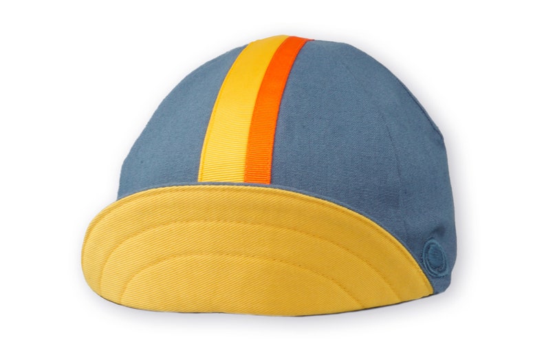 Race to the Sun Cycling Cap by Red Dots Cycling.
A four-panel, vintage blue linen/cotton hat and yellow under brim. Yellow and orange ribbon to the top of the brim. A vintage blue Red Dots embroidered logo on side panel.