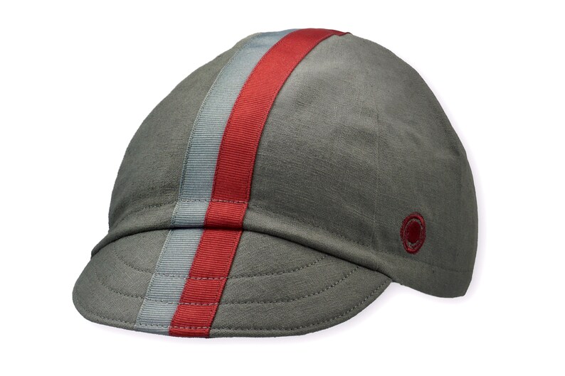 Le Pave Cycling Cap,
A four-panel, Gray linen/cotton hat with a short brim. Gray and burgundy ribbon runs from the back of the cap to the bottom of the brim. Red Dots embroidered burgundy logo on the side panel.
