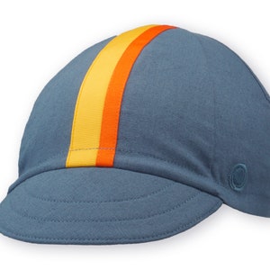 Race to the Sun Cycling Cap by Red Dots Cycling.
A four-panel, vintage blue linen/cotton hat with a short brim. Yellow and orange ribbon to the top of the brim. With a vintage blue Red Dots embroidered logo on the side panel.