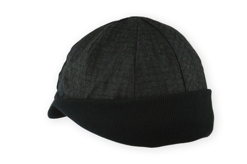 Equinox Winter Cap by Red Dots Cycling. Detail of black, double-layered, bamboo cotton ribbed ear flap in up position. 100% wool plaid fabric, charcoal grey/black plaid and purple accent. Red Dots black logo embroidered on side panel.