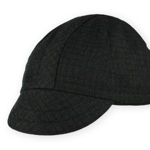 Equinox Winter Cap by Red Dots Cycling. Detail of black, double-layered, bamboo cotton ribbed ear flap in up position. Short brim, 100% wool plaid fabric, charcoal grey/black plaid and purple accent. Red Dots black logo embroidered on side panel.