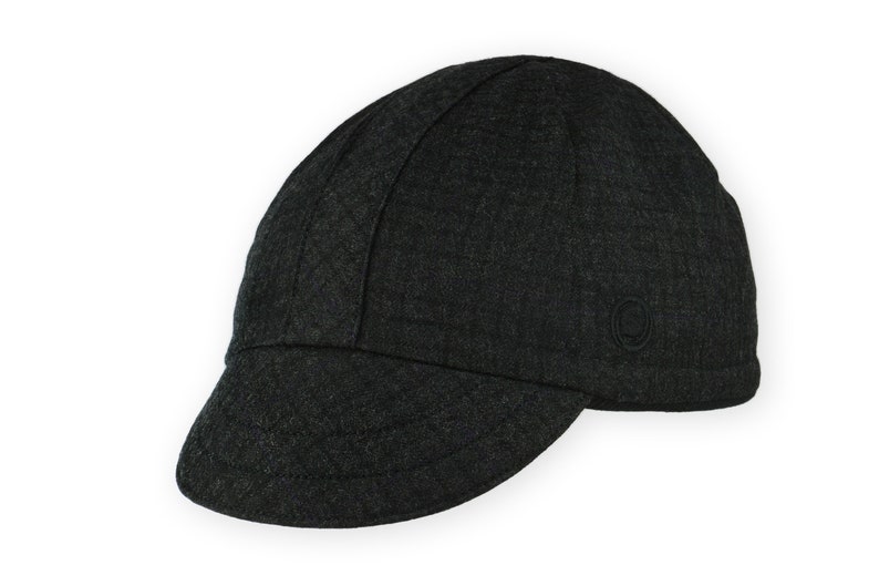 Equinox Winter Cap by Red Dots Cycling. Detail of black, double-layered, bamboo cotton ribbed ear flap in up position. Short brim, 100% wool plaid fabric, charcoal grey/black plaid and purple accent. Red Dots black logo embroidered on side panel.