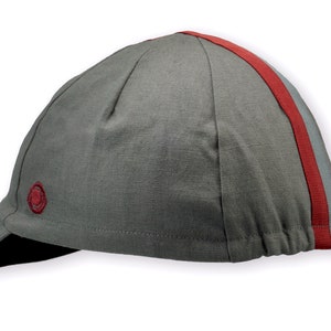 Le Pave Cycling Cap,
A four-panel, Gray linen/cotton hat with black under brim. Gray and burgundy ribbon runs from the back of the cap to the bottom of the brim. Red Dots embroidered burgundy logo on the side panel.