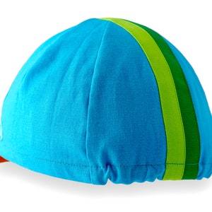 Ardennes Cycling Cap.
A four-panel, Teal linen/cotton hat with orange under brim. Green, lime ribbon from the back of the cap to the bottom of the brim. Red Dots embroidered teal logo on the side panel.