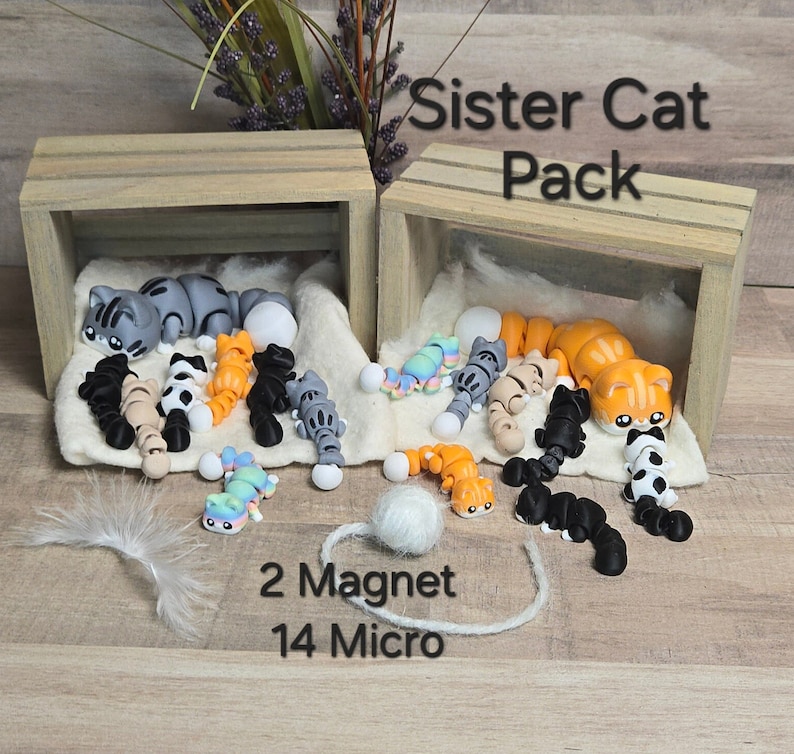 K&ouml;nnte beinhalten: Ein Set aus 16 handgefertigten Katzenfiguren aus Polymer Clay in einer Holzkiste. Das Set enth&auml;lt zwei gr&ouml;&szlig;ere Magnetkatzen und 14 kleinere Mikrokatzen. Die Katzen sind in verschiedenen Posen und Farben, darunter grau, orange, schwarz und wei&szlig;. Der Text "Sister Cat Pack" ist auf der Kiste aufgedruckt.