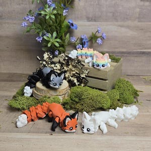 May include: Four handmade polymer clay fox figurines. The foxes are in various poses and have different colored fur. One fox is gray, one is orange, one is white, and one is rainbow colored.