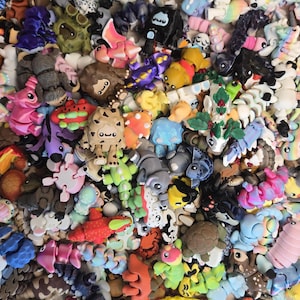 May include: A vibrant assortment of small, colourful figurines depicting animals and abstract shapes. The figurines feature shades of pink, blue, green, yellow, and brown. Some have detailed features, while others are simpler. The overall aesthetic is whimsical and playful, with a variety of designs.
