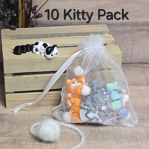 K&ouml;nnte beinhalten: Eine wei&szlig;e Organzabtasche gef&uuml;llt mit 10 kleinen, bunten Katzenfiguren. Die Tasche ist mit einem wei&szlig;en Band gebunden. Der Text "10 Kitty Pack" ist &uuml;ber der Tasche sichtbar.