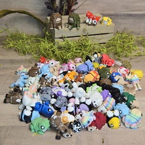 May include: A selection of colourful miniature animal figurines, including frogs, deer, and bears, in various poses and colours. Some figurines are on a wooden crate with greenery.