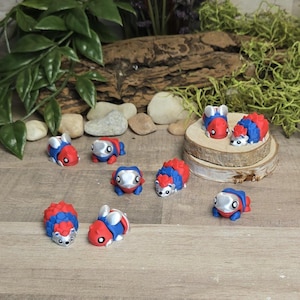 May include: A collection of small, colorful figurines resembling hedgehogs and other creatures. The figurines are primarily red, blue, and silver, with detailed features. Some are displayed on small wooden platforms, creating a whimsical scene.