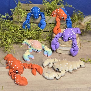 May include: Six colourful lobster figurines with articulated legs and spots. The lobsters are in various colours, including blue, orange, purple, pink, and brown.