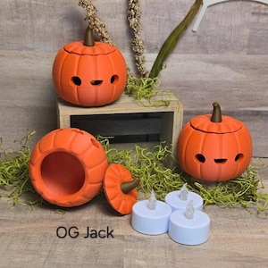 May include: Orange pumpkin-shaped containers with smiling faces and removable lids. The pumpkins have brown stems and are displayed with white LED tea lights. The text "OG Jack" is visible on the bottom left.