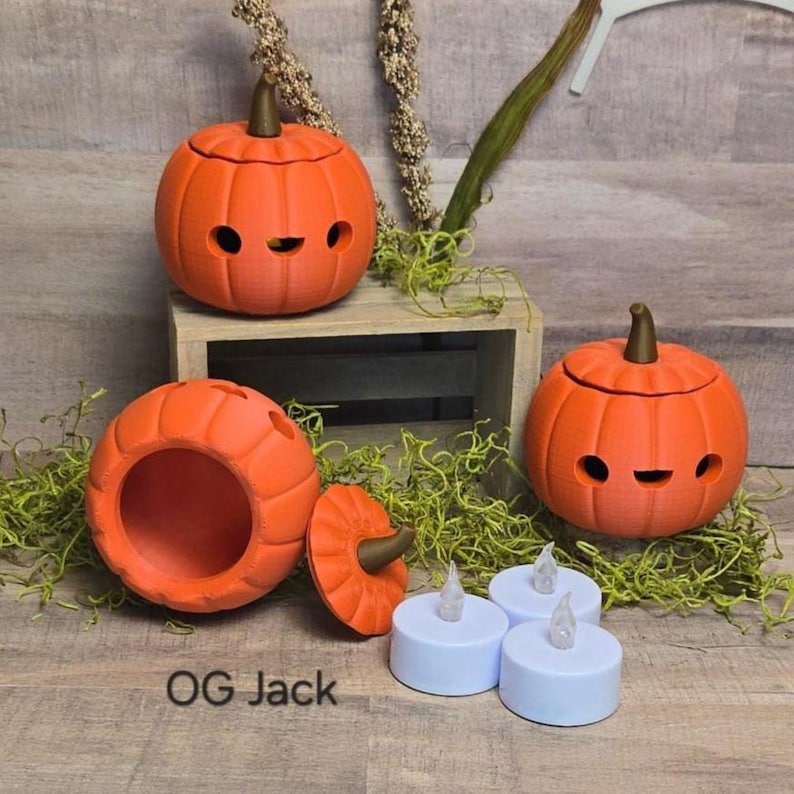May include: Orange pumpkin-shaped containers with smiling faces and removable lids. The pumpkins have brown stems and are displayed with white LED tea lights. The text "OG Jack" is visible on the bottom left.