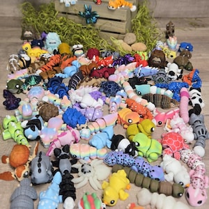 May include: A selection of colourful, handcrafted polymer clay figurines, including various animals and creatures. The figurines are in a variety of colours, including blue, orange, pink, and green. Some are segmented, resembling caterpillars or worms.