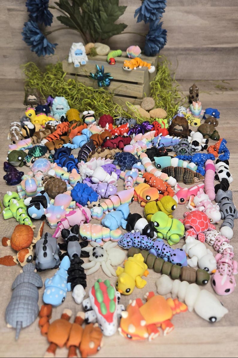 May include: A selection of colourful, handcrafted polymer clay figurines, including various animals and creatures. The figurines are in a variety of colours, including blue, orange, pink, and green. Some are segmented, resembling caterpillars or worms.