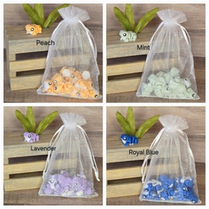 May include: Four organza bags filled with small frog figurines. The bags are labeled with the colors of the frogs: Peach, Mint, Lavender, and Royal Blue.