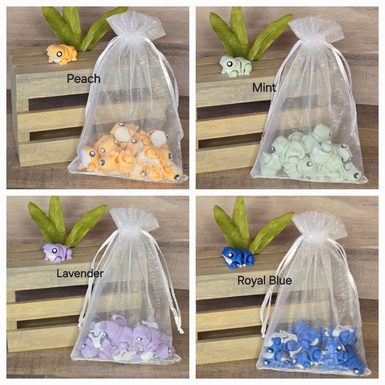 May include: Four organza bags filled with small frog figurines. The bags are labeled with the colors of the frogs: Peach, Mint, Lavender, and Royal Blue.