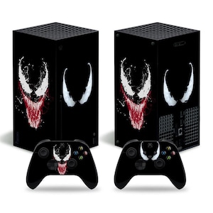 May include: A black Xbox Series X console and controller with a Venom graphic design. The console has a black and white image of Venom's face with red teeth and a white background. The controller has a similar design with Venom's face in the center.