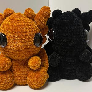 May include: Two crocheted plush dragon toys. One is orange and the other is black. Both have large black eyes.