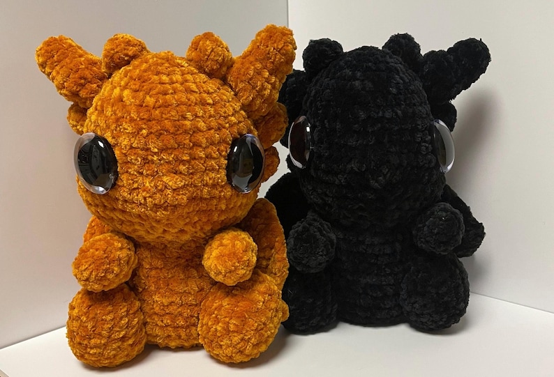 May include: Two crocheted plush dragon toys. One is orange and the other is black. Both have large black eyes.