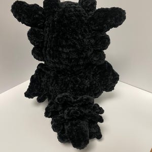 May include: Black crocheted plush toy shaped like a dragon with a spiky head and a curled tail.