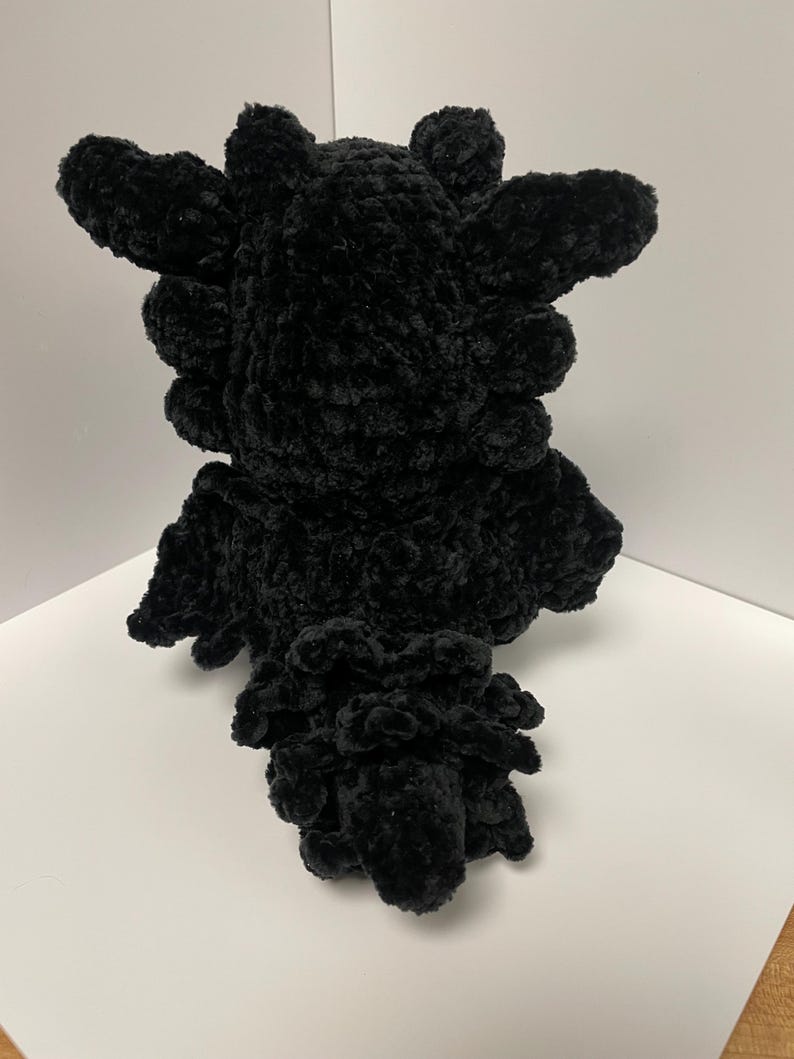 May include: Black crocheted plush toy shaped like a dragon with a spiky head and a curled tail.