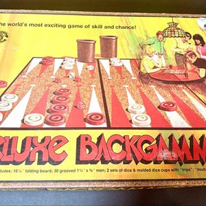 May include: A Deluxe Backgammon board game box with a yellow cover featuring the text The world's most exciting game of skill and chance! and Deluxe Backgammon. The box shows a game board, dice, cups, and an illustration of people playing.
