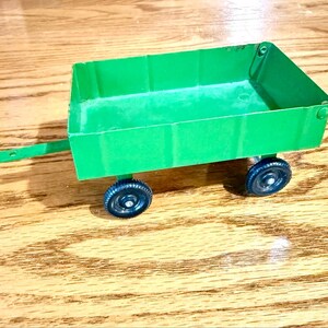 May include: A small, bright green toy wagon with a rectangular bed and a pull handle. The wagon has two black wheels and is set against a wooden surface. The wagon is a classic toy.