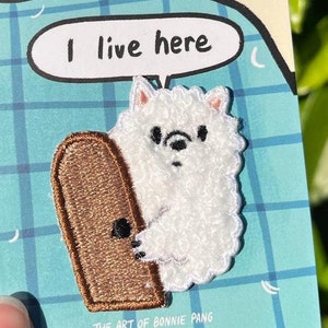 May include: A white fluffy animal peeking out from behind a brown door with the text "I live here" in a speech bubble above. The text "THE ART OF BONNIE PANG" is at the bottom of the image.