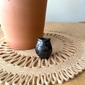 May include: A small, black, carved stone owl figurine featuring intricate floral and geometric patterns etched into its surface. The owl has prominent circular eyes and a detailed chest design, showcasing a smooth, dark, polished finish throughout.
