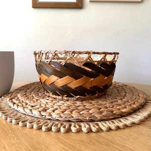 Round open basket with wide sides perfect for fruit or bread. Thick bands of brown leaves woven along the sides. Dark brown with lighter brown bands. Nice rustic, boho style.