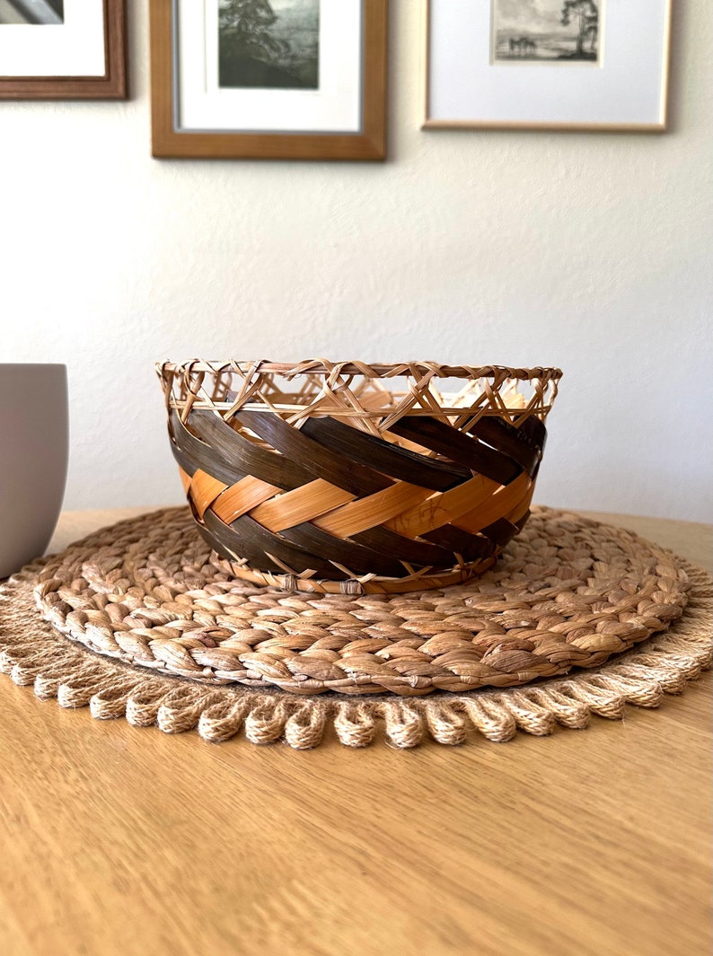 Round open basket with wide sides perfect for fruit or bread. Thick bands of brown leaves woven along the sides. Dark brown with lighter brown bands. Nice rustic, boho style.