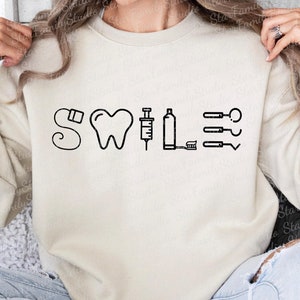 May include: A white sweatshirt with a black graphic design that says "Smile" with dental tools and a tooth.
