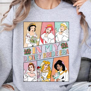 Peut inclure: Un sweat-shirt gris avec un imprim&eacute; graphique de princesses Disney en robes de mari&eacute;e. Le texte "In My Disney Bride Era" est imprim&eacute; sur le graphique.