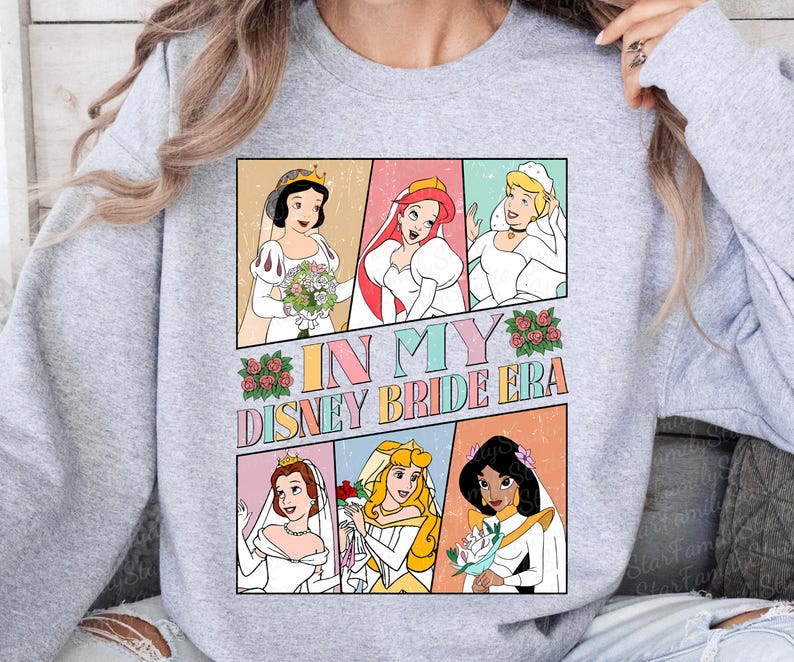 Peut inclure: Un sweat-shirt gris avec un imprim&eacute; graphique de princesses Disney en robes de mari&eacute;e. Le texte "In My Disney Bride Era" est imprim&eacute; sur le graphique.