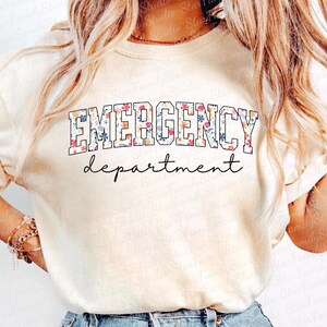 K&ouml;nnte beinhalten: Ein wei&szlig;es T-Shirt mit einem floralen Druckdesign. Der Text "EMERGENCY department" ist in Schwarz auf dem Shirt gedruckt.