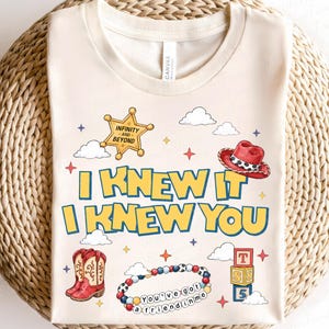 Może przedstawiać: Kremowy t-shirt z nadrukiem graficznym zawierającym tekst I KNEW IT I KNEW YOU, ż&oacute;łtą gwiazdę szeryfa z napisem INFINITY AND BEYOND, czerwony kapelusz kowbojski, czerwone kowbojki, bransoletkę z koralik&oacute;w z napisem YOU'VE GOT A FRIEND IN ME i klocki.