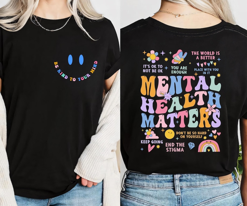 Puede incluir: Camiseta negra con un dise&ntilde;o de arco&iacute;ris que dice "La salud mental importa" y una carita sonriente con el texto "S&eacute; amable con tu mente".