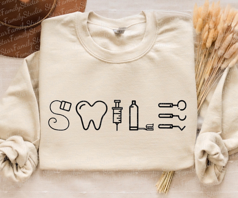 May include: A beige sweatshirt with the word "SWILE" printed in black. The word is made up of dental tools, including a toothbrush, syringe, floss, and a tooth.