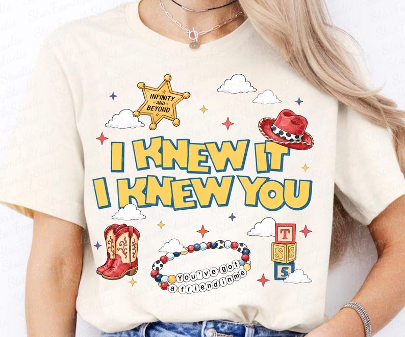 Może przedstawiać: Kremowy t-shirt z napisem "I KNEW IT I KNEW YOU" w kolorze ż&oacute;łtym z niebieskim obrysem. Grafiki przedstawiają złotą gwiazdę szeryfa, czerwony kowbojski kapelusz, czerwone kowbojki, bransoletkę z koralik&oacute;w z napisem "You've got a friend in me" oraz klocki.